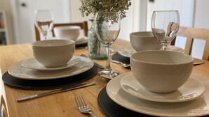 A dining table set with white bowls, plates, and cutlery, a vase with flowers, and a wine glass. - 3 Glantraeth Farm Cottage. Pet friendly, ideal base to explore Anglesey. (Trefdraeth, Bodorgan, Anglesey)