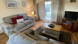 A living room with a grey sofa, a coffee table, and a TV stand. - 3 Glantraeth Farm Cottage. Pet friendly, ideal base to explore Anglesey. (Trefdraeth, Bodorgan, Anglesey)