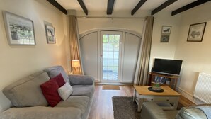 A living room with a grey sofa, a leather armchair, a wooden coffee table, and a TV stand. - 3 Glantraeth Farm Cottage. Pet friendly, ideal base to explore Anglesey. (Trefdraeth, Bodorgan, Anglesey)
