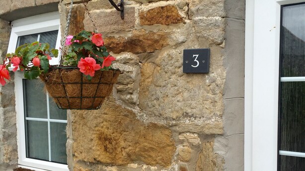 A stone building with a hanging flower basket and a door number sign. - 3 Glantraeth Farm Cottage. Pet friendly, ideal base to explore Anglesey. (Trefdraeth, Bodorgan, Anglesey)