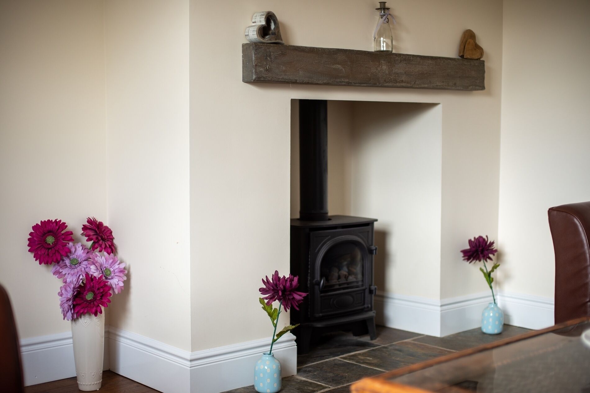A room with a fireplace, two vases with flowers, and a wooden shelf above the fireplace.