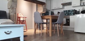 A compact kitchen with a dining table, two chairs, a white refrigerator, and a stone wall.