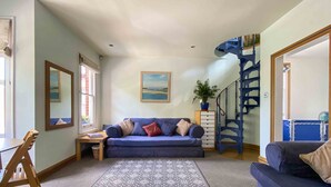 Ein Wohnzimmer mit einem blauen Sofa, einem gemusterten Teppich, einem Holzstuhl, einem kleinen Tisch und einer Treppe mit blauen Geländern.