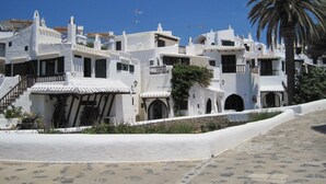 A coastal village with white buildings, a palm tree, and a paved walkway. - Detached Modern Family Villa with Private Pool in Quiet Location Close to Beach (Sant Lluis)