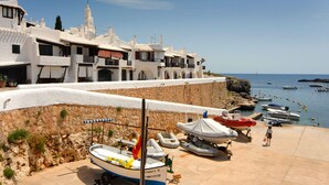 A coastal building with a stone wall, a white facade, and a balcony. - Detached Modern Family Villa with Private Pool in Quiet Location Close to Beach (Sant Lluis)