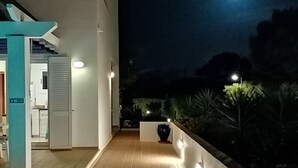 A nighttime view of a modern building with a tiled patio, a pool, and a well-lit pathway leading to the entrance. - Detached Modern Family Villa with Private Pool in Quiet Location Close to Beach (Sant Lluis)