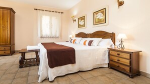 A neatly arranged bedroom with a large bed, bedside tables, a wooden wardrobe, and a window with curtains. - Country house with private pool and panoramic views and accessible (Santa Margalida)