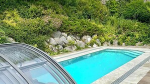 A swimming pool with a glass enclosure, surrounded by a stone wall and lush greenery. - Hillside villa with private pool (Altmünster)