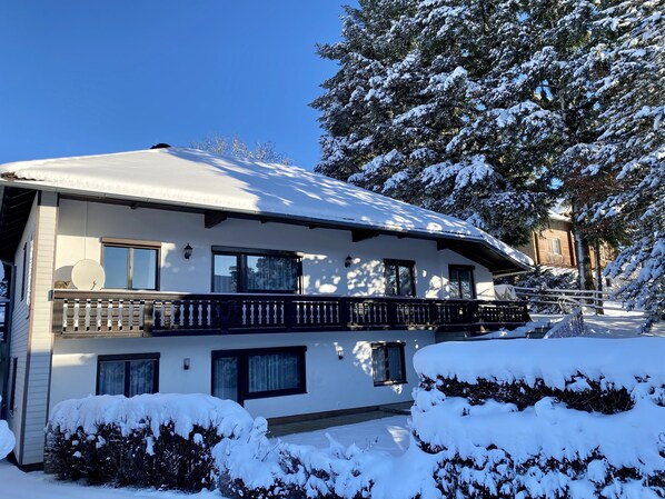 A two-story building with a balcony, snow-covered roof, and surrounding trees.