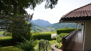 A balcony with a view of mountains, a garden with various plants, and a building with a tiled roof. - Hillside villa with private pool (Altmünster)