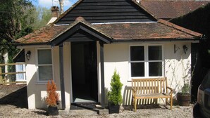 A small, single-story building with a pitched roof, a front door, and a bench outside. - Amberfold Lodge, Heyshott near Midhurst (Midhurst)