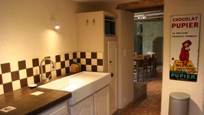 A kitchen with a checkered backsplash, a sink, cabinets, and a poster advertising chocolate. - Gîte Nature In Aveyron (La Bastide-Pradines)