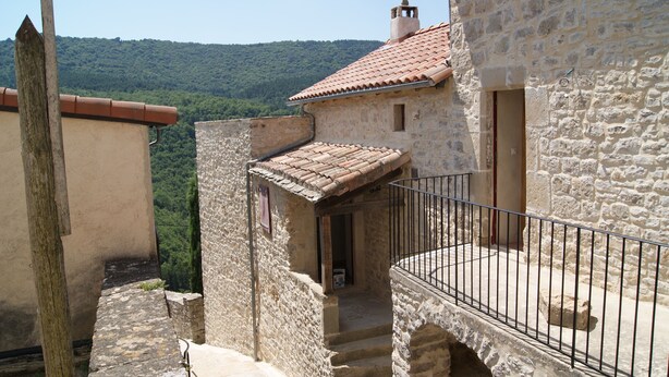 A stone building with a tiled roof, a small balcony with a metal railing, and a staircase leading to an upper level. - Gîte Nature In Aveyron (La Bastide-Pradines)