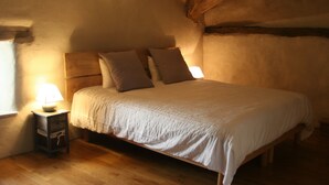 A cozy bedroom with a wooden bed, a nightstand with a lamp, and a sloped ceiling. - Gîte Nature In Aveyron (La Bastide-Pradines)