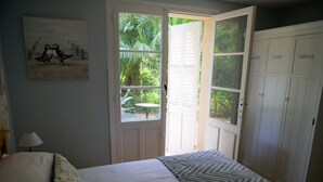 Une chambre avec deux lits, une fenêtre avec des volets, une porte sur laquelle sont indiqués les noms des pièces, et un tableau accroché au mur.