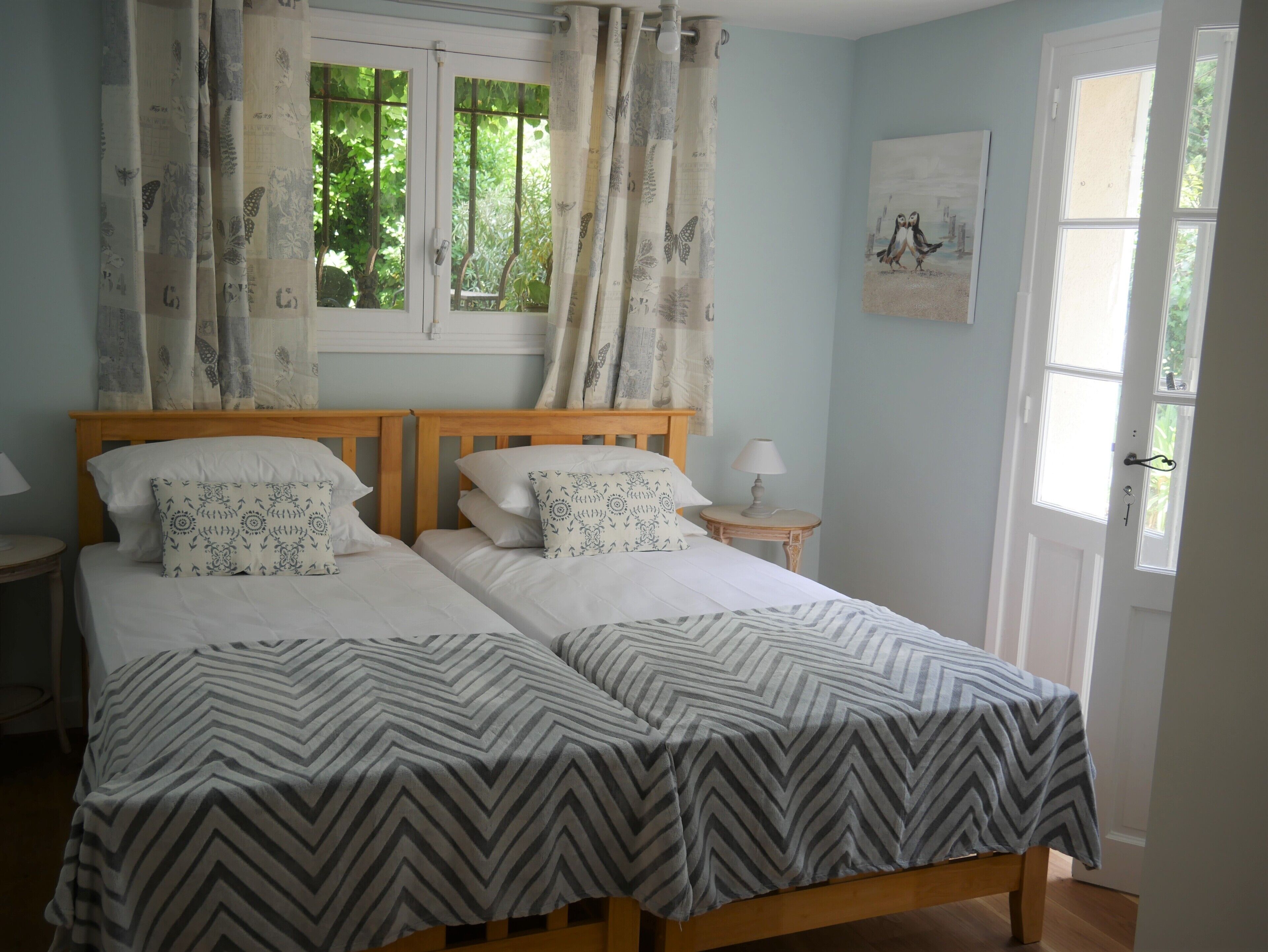 A double bed with patterned pillows, a bedside table with a lamp, and a window with curtains.