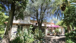Un bâtiment rustique en pierre, doté d’un toit en tuiles, entouré d’une végétation luxuriante et de cactus.
