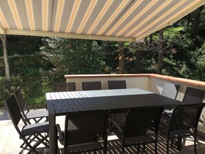 An outdoor patio with a table and chairs, surrounded by a wooden deck and a covered area with striped fabric.