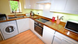 A compact kitchen with a washing machine, oven, microwave, and wooden countertops.