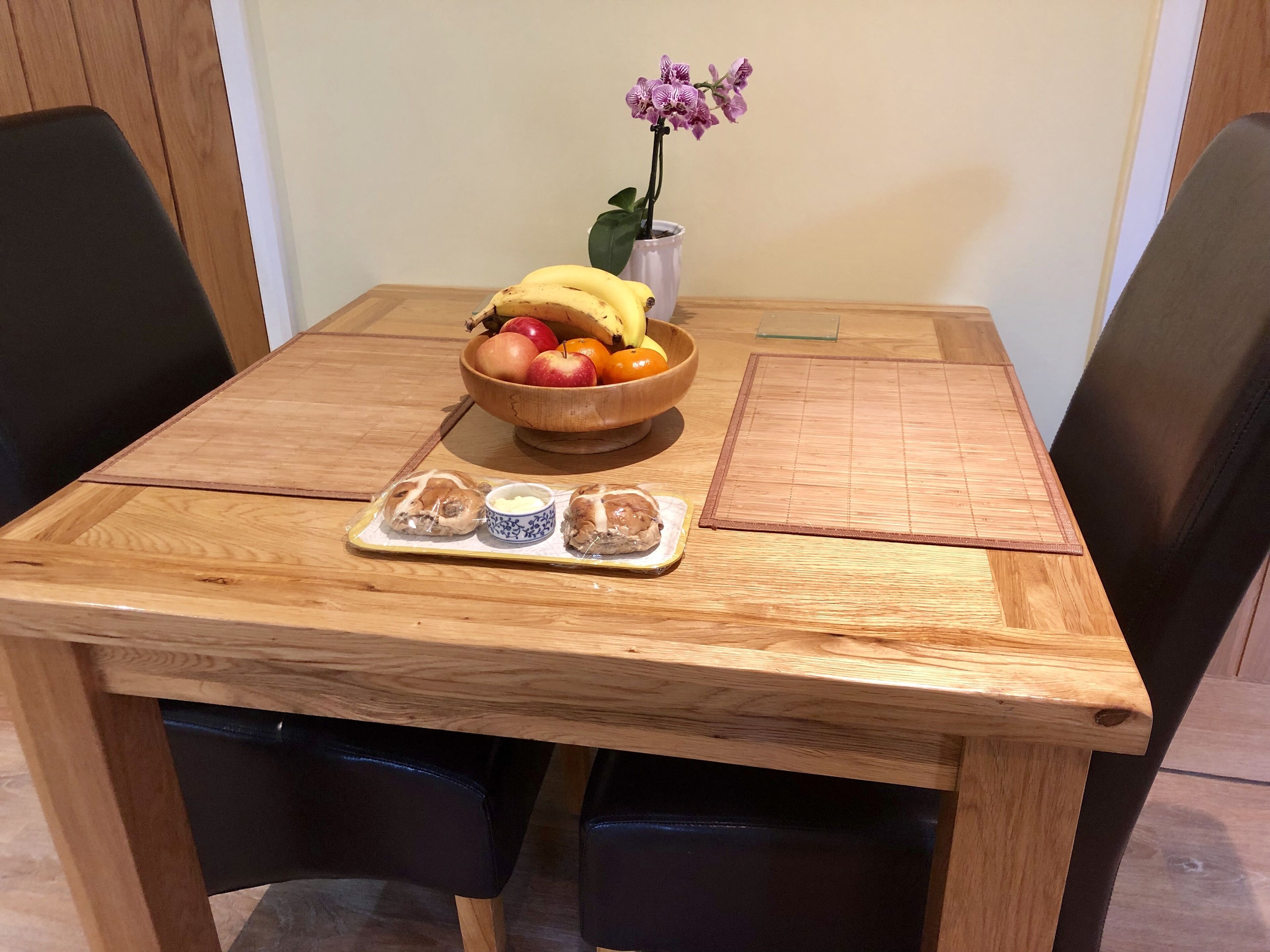 Ein Holztisch mit einer Obstschale, einer kleinen Topfpflanze und einer Auswahl an Gebäck.
