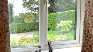 A window with two rabbit figurines on the sill, a white window frame, and a view of a garden with yellow flowers and green hedges.