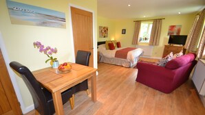 A room with a wooden dining table, a red sofa, a bed with a white duvet, and a TV on a stand.