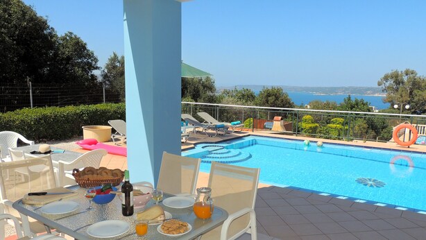 Un espace aménagé au bord de la piscine, avec une table pour deux, une chaise et une vue sur la piscine et la mer.