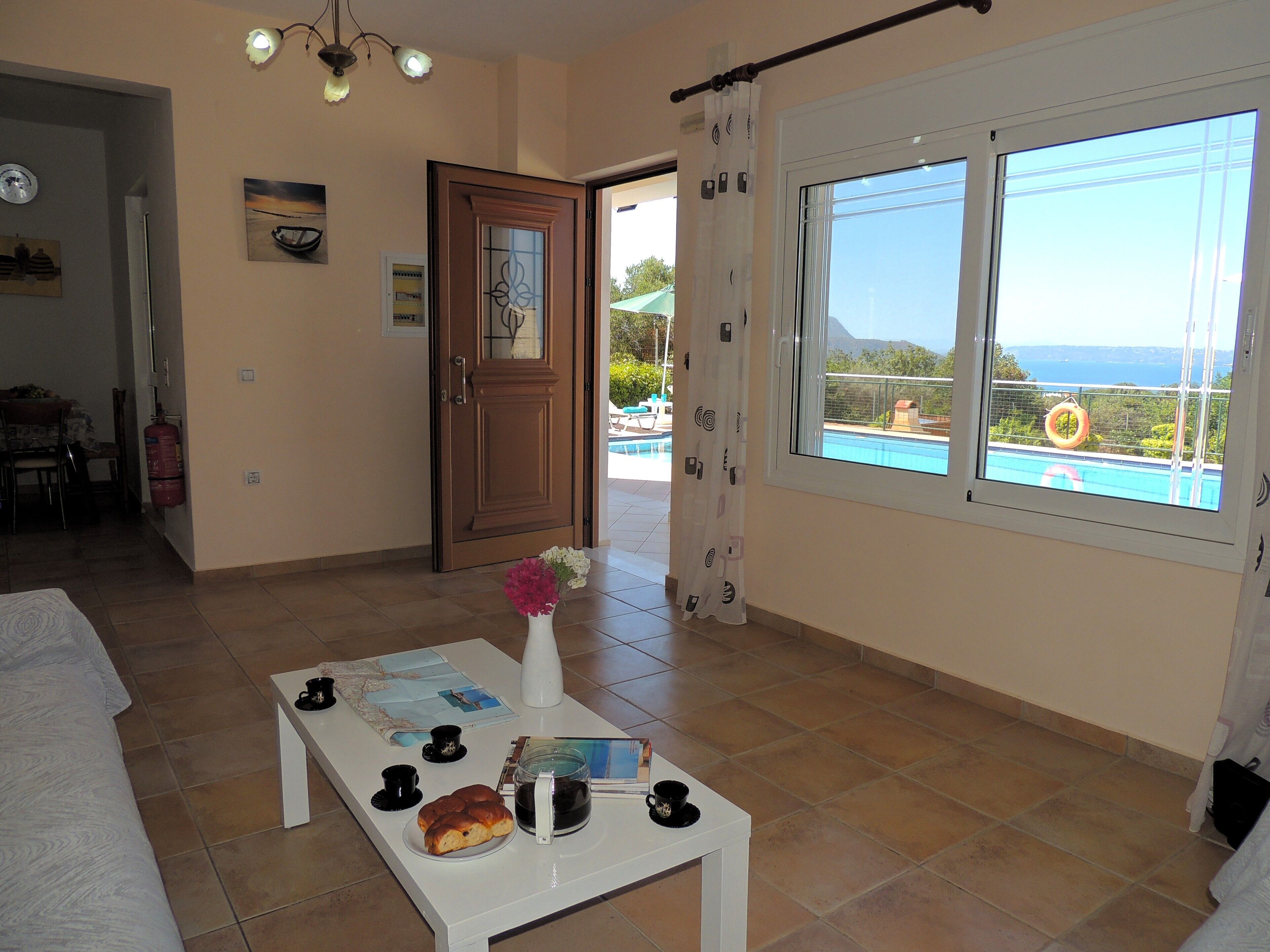 A room with a bed, a coffee table with a map, a coffee cup, and a pastry. There is a window with a view of a pool and mountains.