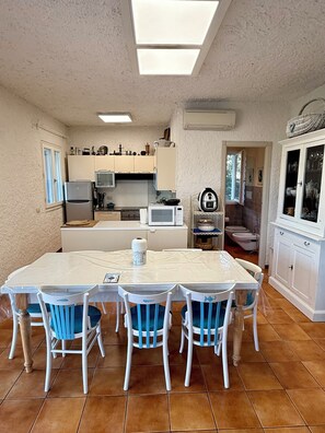 Une cuisine compacte avec un coin repas, des meubles blancs et un sol carrelé.