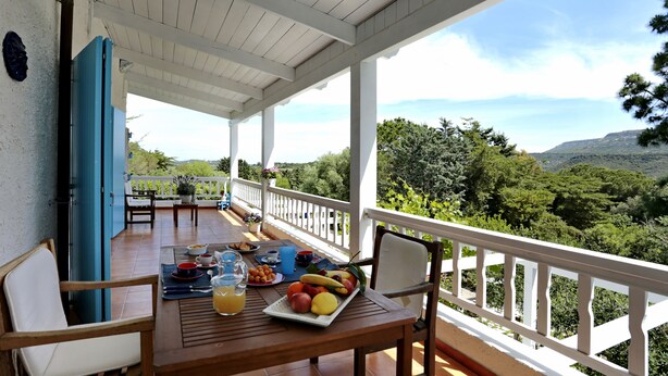 A covered outdoor dining area with a table set for breakfast, overlooking a lush landscape.