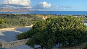 Eine Küstenlandschaft mit einer Steinmauer, einem Baum und Blick auf das Meer und ferne Hügel.