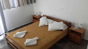 Ein ordentlich bezogenes Bett mit brauner Bettdecke und weißen Kissen, Nachttische aus Holz mit Lampen und ein gefliester Boden.