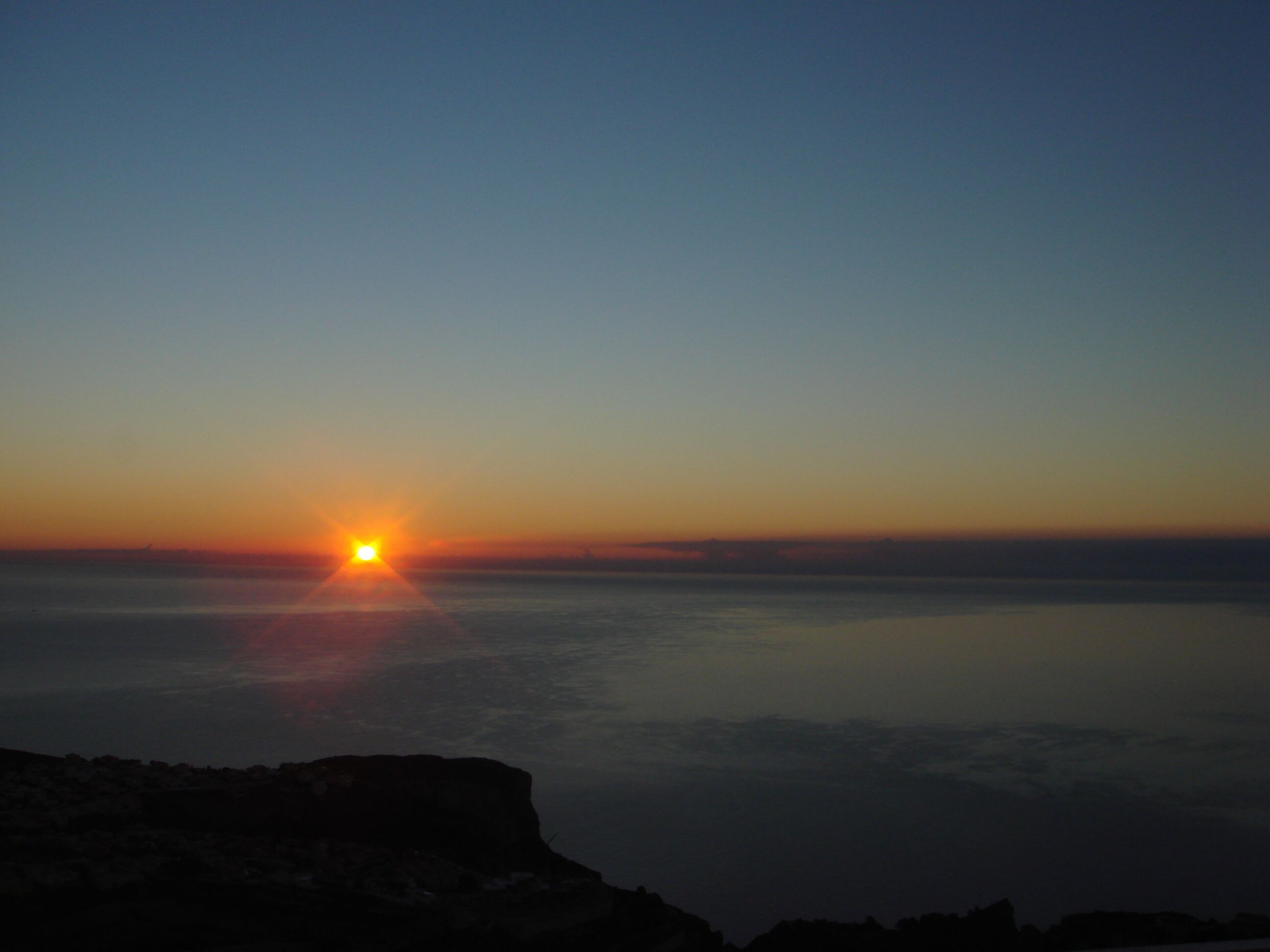 A sunset over a calm sea with a rocky coastline.