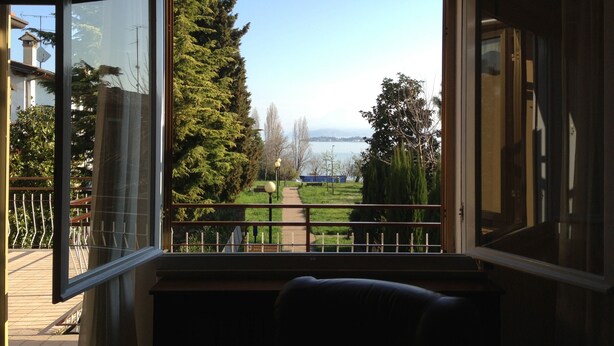 A room with a large window offering a view of a park, a pathway, and a body of water.