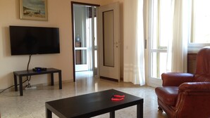 A living room with a flat-screen TV, a small table, a leather armchair, and a door leading to another room.