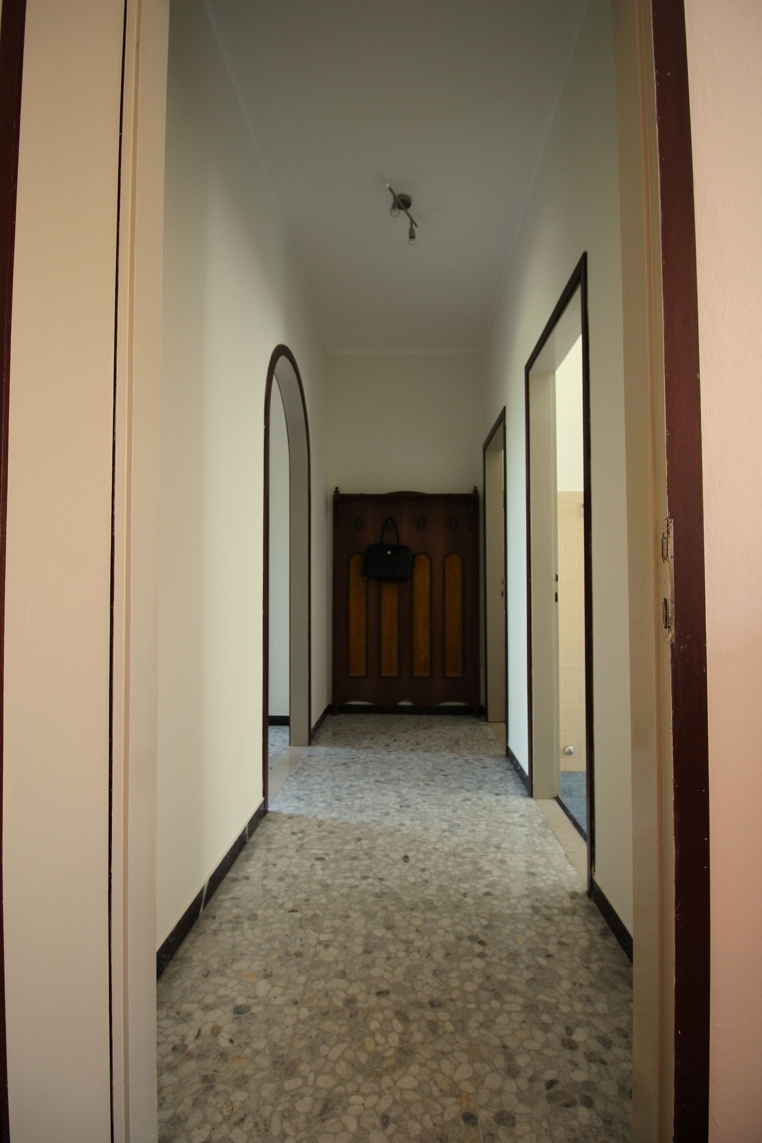 A hallway with a tiled floor, wooden door frames, and a ceiling fan.
