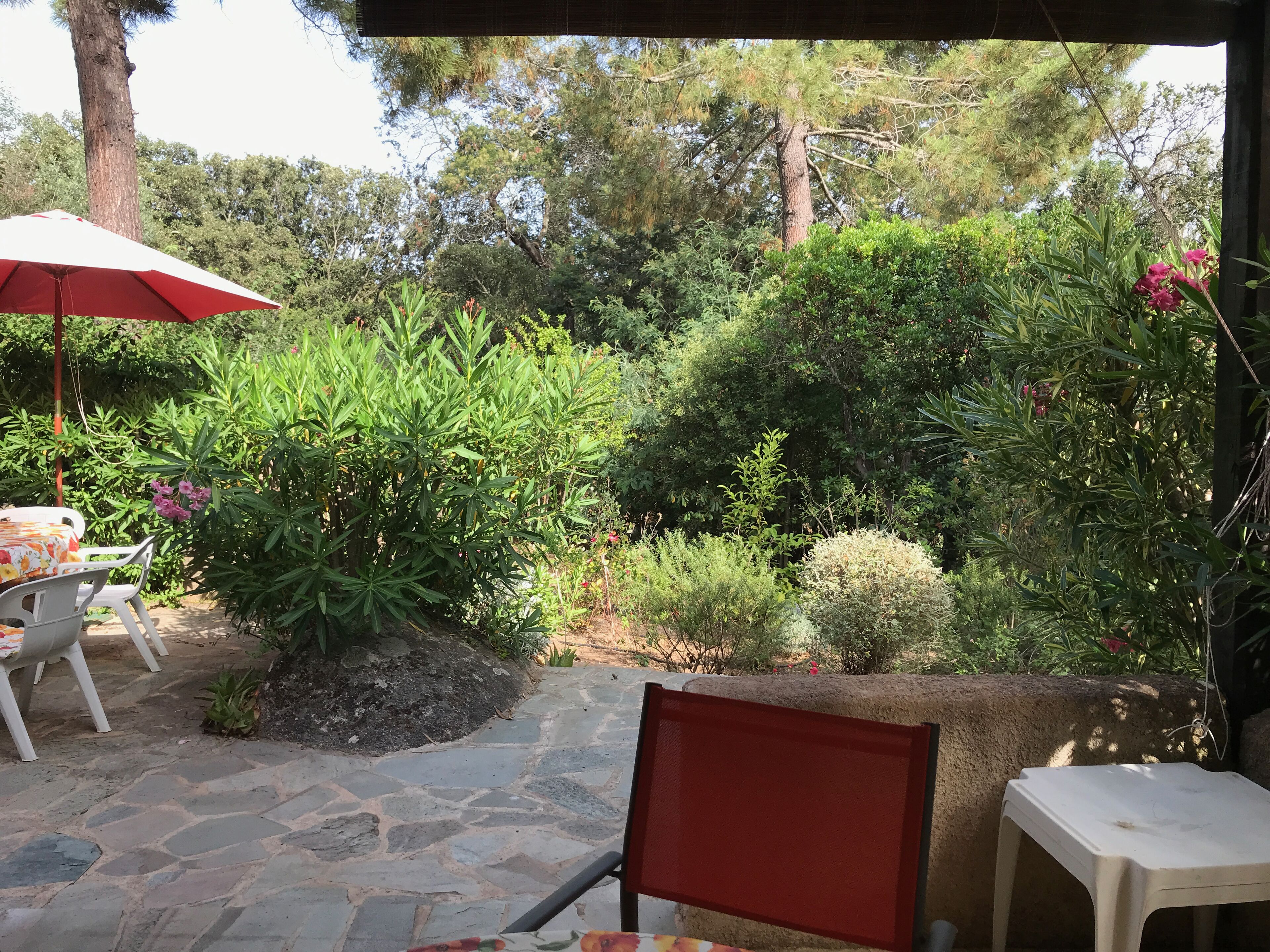 Un espace patio avec un sol en pierre, une table entourée de chaises et un parasol rouge.