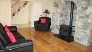 A living room with a stone fireplace, a black leather sofa with red cushions, and a staircase leading to another room.