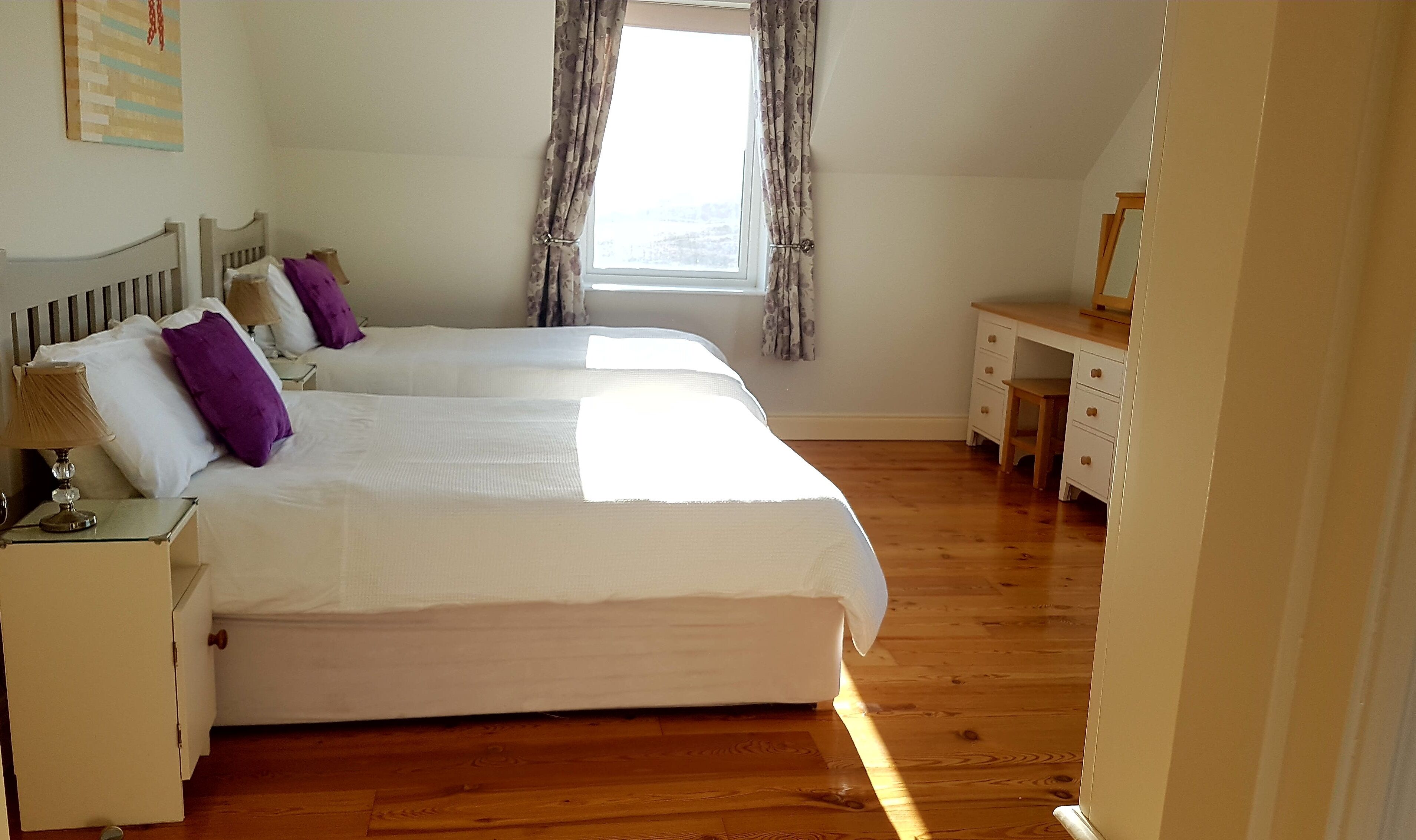 Een slaapkamer met twee bedden, een nachtkastje, een dressoir en een raam met gordijnen.