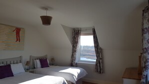 A bedroom with two beds, a window with curtains, a hanging light fixture, and a wall-mounted artwork.