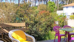 Une terrasse extérieure avec des fauteuils en osier et une table en verre, entourée d’une végétation luxuriante et de grands arbres.