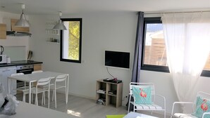 Une pièce moderne et bien éclairée, comprenant un coin repas, un téléviseur fixé au mur et une fenêtre avec des rideaux.