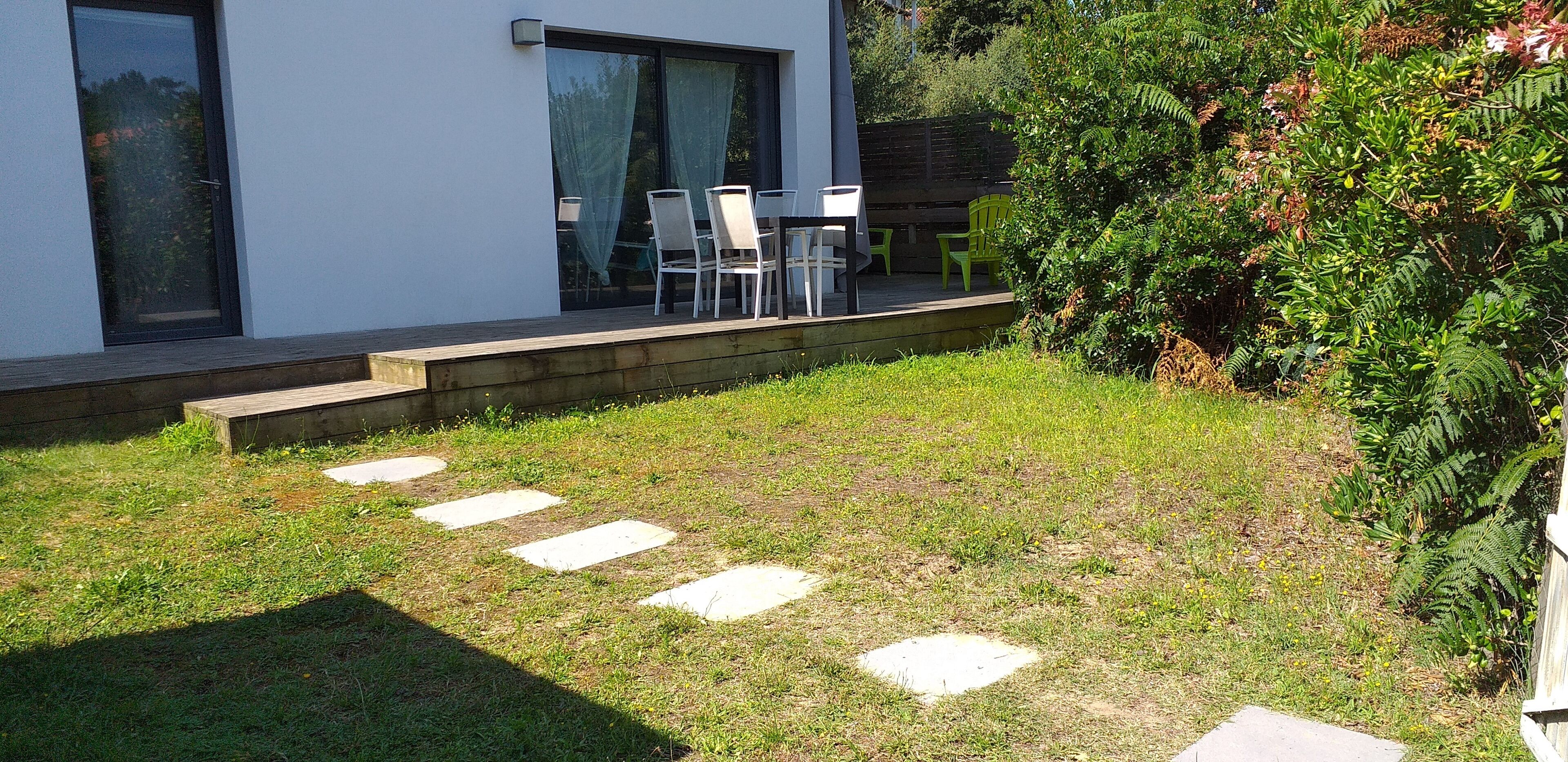 A modern house with a patio, outdoor seating, and a well-maintained lawn.