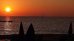 Een zonsondergang boven een rustige zee met een boot in de verte en strandparasols.
