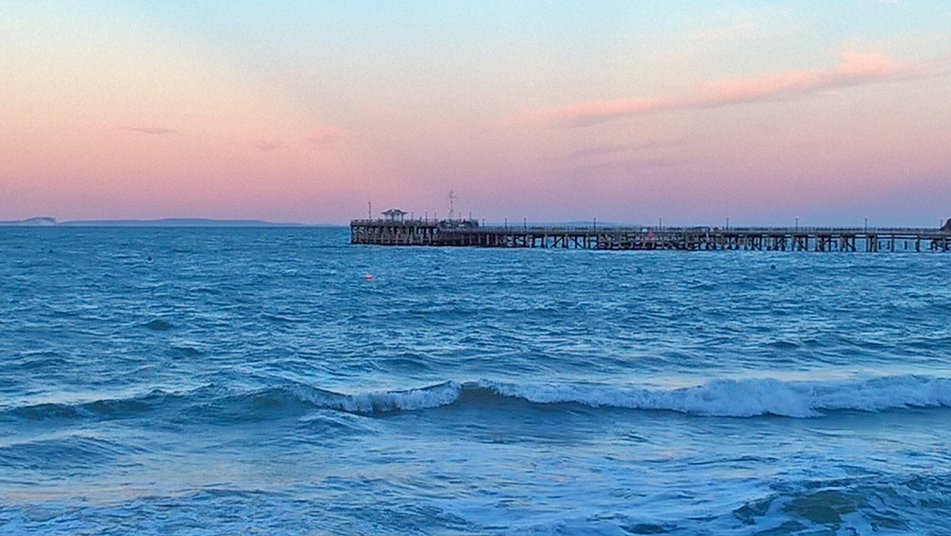 A pier extending into the sea with waves crashing against it.