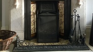 Ein Kamin mit einem Spiegel darüber, Kerzen auf beiden Seiten und eine Vase mit roten Blumen in der Mitte.