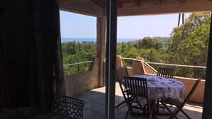 Un balcón con mesa y sillas, con vistas a un paisaje pintoresco con árboles y una lejana perspectiva.