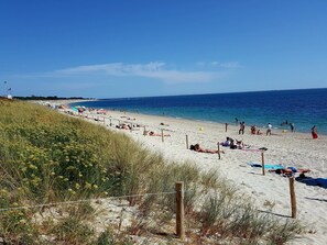 Una playa con gente tomando el sol y nadando, una orilla arenosa y un cielo azul despejado.