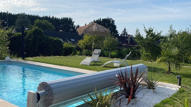 Una piscina con un moderno sistema di filtraggio, circondata da un giardino curato con diverse piante e un ombrellone di paglia.