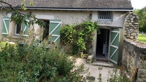 Una casa in pietra rustica con persiane verdi, una piccola finestra e un'uscita che dà su un giardino.